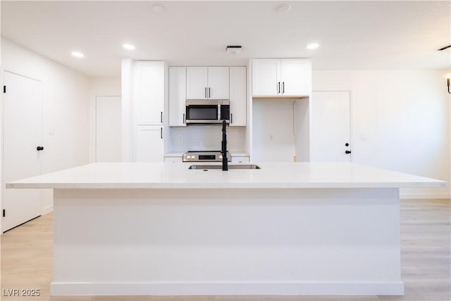 508 S Jones Blvd, Las Vegas, NV 89107 - kitchen featuring stainless steel microwave, an island with sink, white cabinets, light wood-type flooring, and light countertops