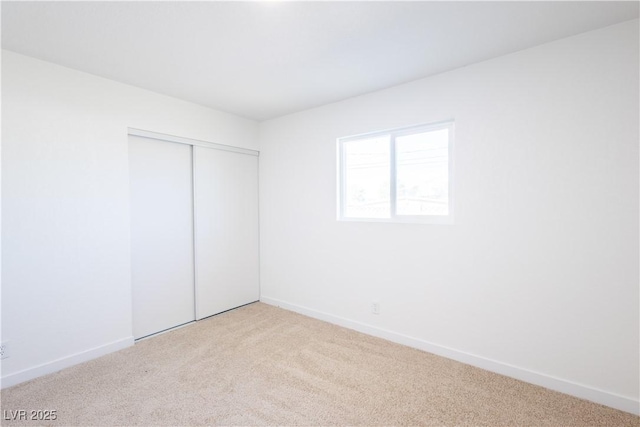 unfurnished bedroom with a closet, light colored carpet, and baseboards