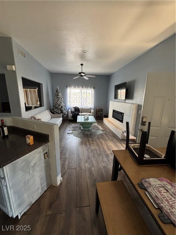 living room with a glass covered fireplace, ceiling fan, dark wood-style floors, and a textured ceiling