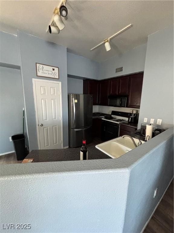 kitchen featuring black microwave, dark wood-style floors, freestanding refrigerator, range with gas cooktop, and rail lighting