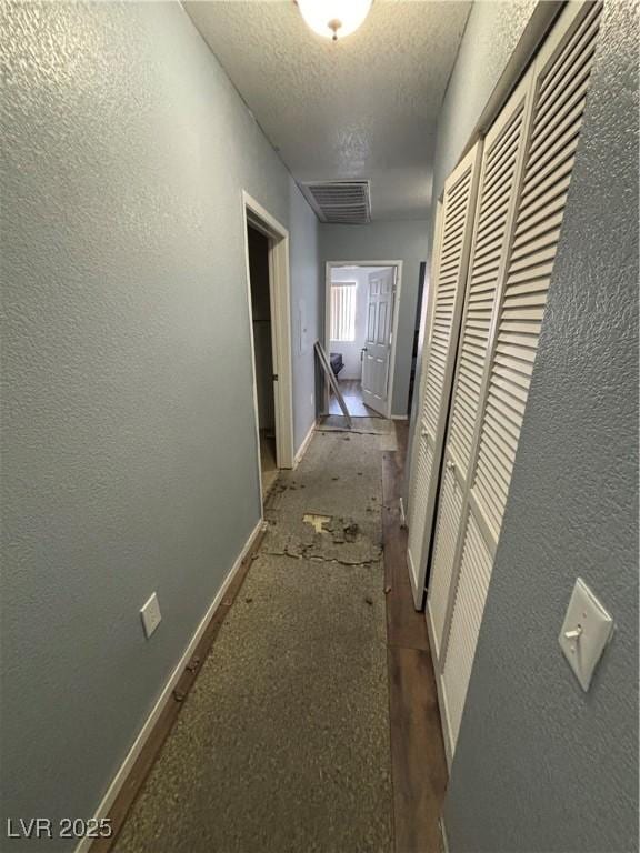 hall featuring baseboards, visible vents, a textured ceiling, and a textured wall