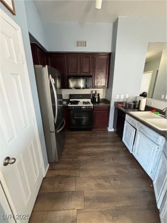 kitchen with black microwave, visible vents, dark wood-style floors, freestanding refrigerator, and gas stove