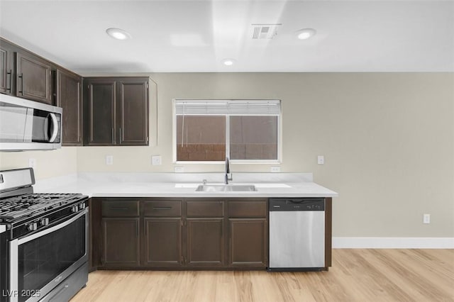 kitchen featuring a sink, stainless steel appliances, light countertops, dark brown cabinetry, and light wood-type flooring