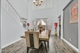 dining room with wood finished floors, stairway, baseboards, a chandelier, and a high ceiling