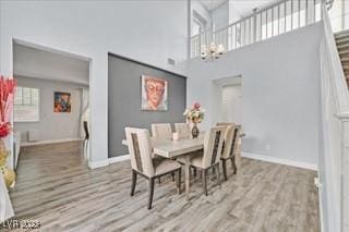 dining area featuring baseboards, a high ceiling, wood finished floors, and a notable chandelier