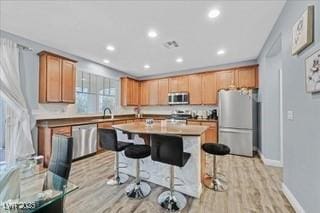 kitchen featuring baseboards, light wood-style floors, a breakfast bar area, a center island with sink, and stainless steel appliances