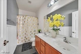 bathroom featuring double vanity, a sink, a wainscoted wall, toilet, and a shower with shower curtain