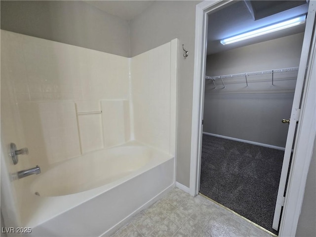 bathroom with a walk in closet, tub / shower combination, and baseboards