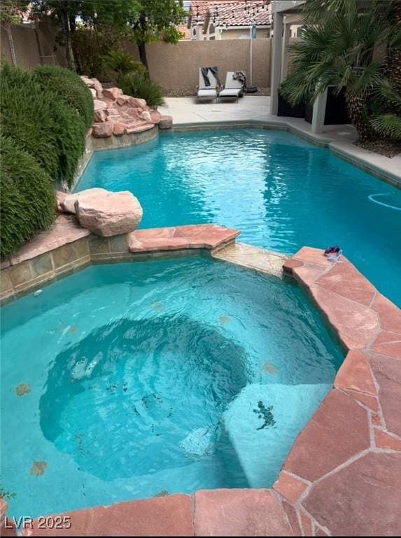 view of swimming pool with fence and a pool with connected hot tub