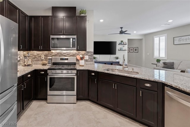 kitchen with a sink, stainless steel appliances, a ceiling fan, light stone counters, and open floor plan