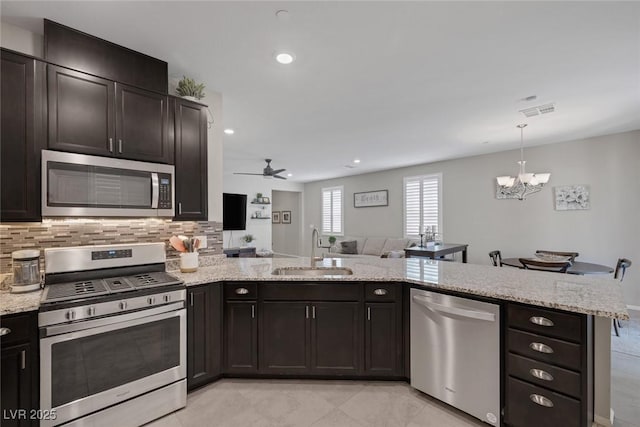 kitchen featuring light stone counters, appliances with stainless steel finishes, a sink, a peninsula, and open floor plan