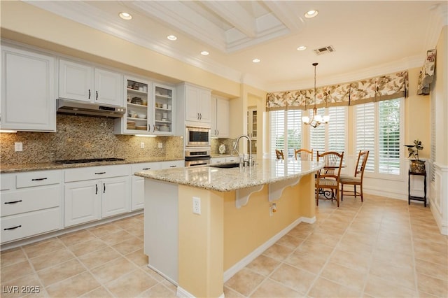 kitchen with a sink, stainless steel appliances, under cabinet range hood, visible vents, and ornamental molding