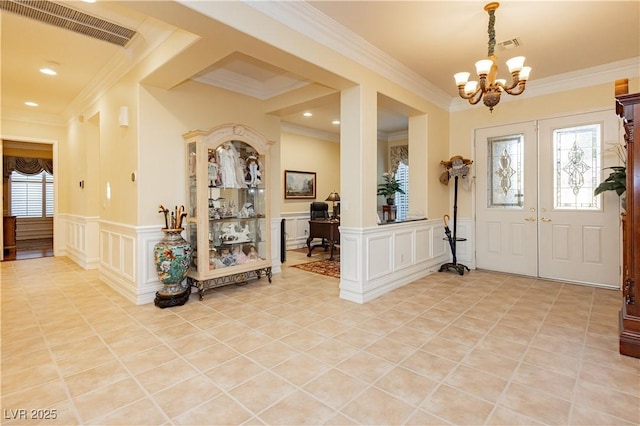 entryway with crown molding, visible vents, a chandelier, a decorative wall, and wainscoting