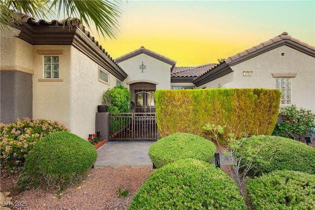 view of exterior entry with stucco siding, fence, a gate, and a tile roof