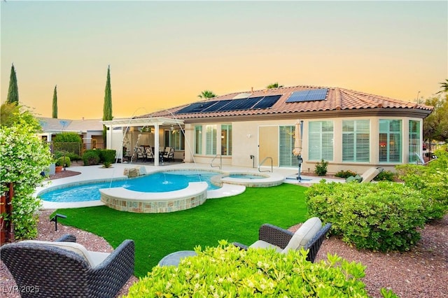 back of property with a tiled roof, a yard, roof mounted solar panels, a pool with connected hot tub, and a patio area