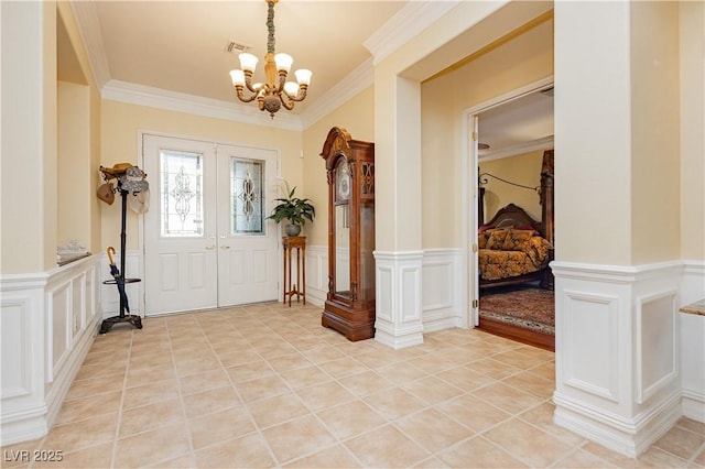 foyer with visible vents, a chandelier, a decorative wall, and ornamental molding