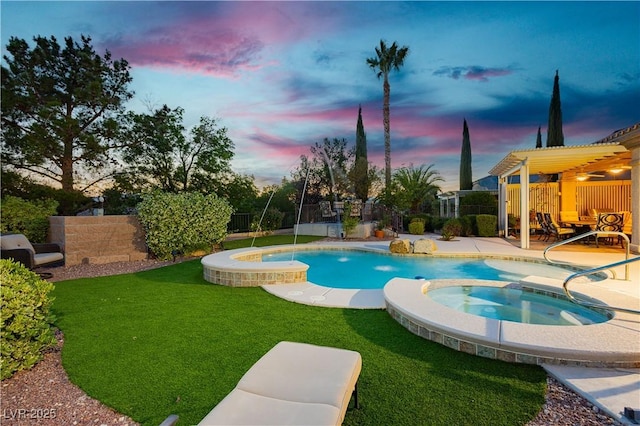 pool at dusk with a yard, a patio area, a pool with connected hot tub, and a fenced backyard