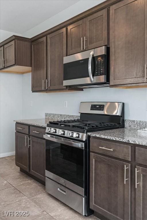 kitchen featuring stainless steel appliances, dark brown cabinets, light stone countertops, and light tile patterned floors