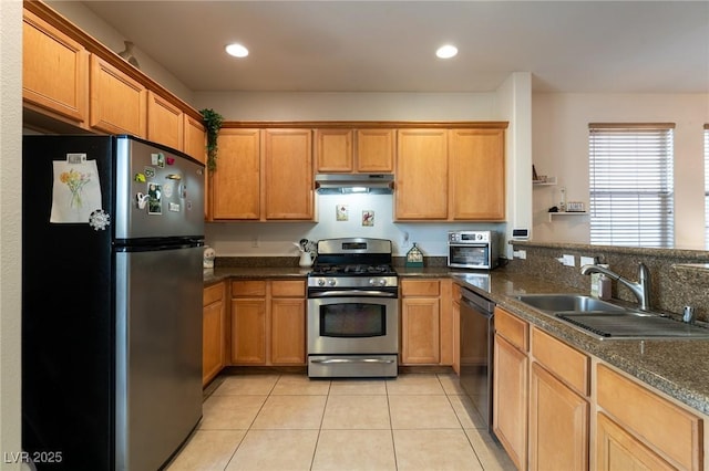 kitchen with under cabinet range hood, brown cabinets, a sink, appliances with stainless steel finishes, and light tile patterned floors