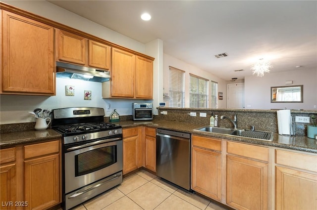 kitchen with appliances with stainless steel finishes, a sink, light tile patterned floors, a chandelier, and under cabinet range hood