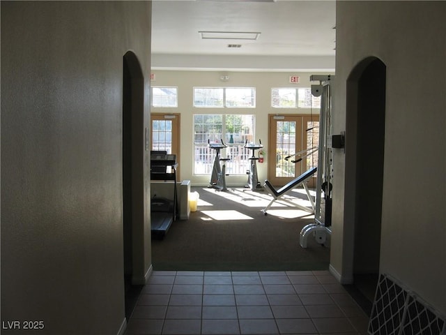 corridor featuring tile patterned flooring, carpet flooring, baseboards, and arched walkways