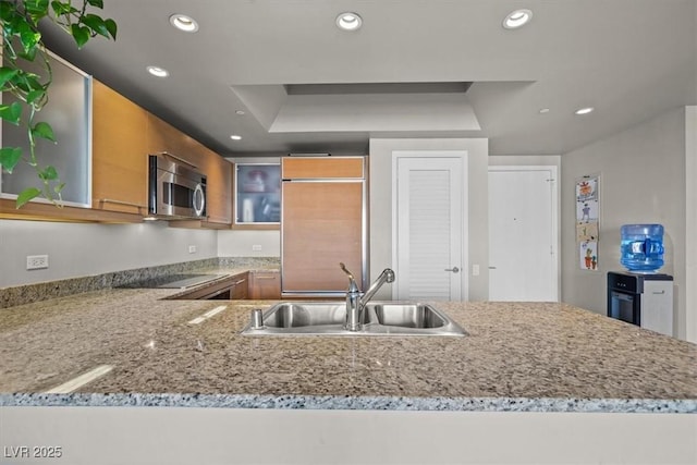 kitchen with recessed lighting, stainless steel microwave, brown cabinets, black electric cooktop, and a sink