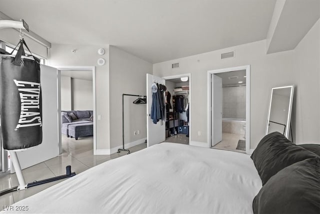 tiled bedroom with a walk in closet, visible vents, and baseboards