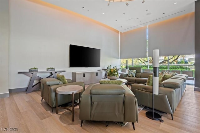 living room with a towering ceiling, light wood-style flooring, and baseboards