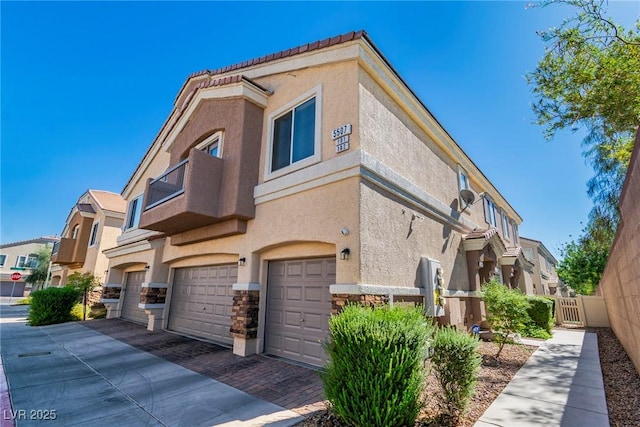 view of side of home featuring fence, stone siding, decorative driveway, stucco siding, and a garage