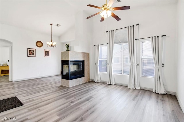 unfurnished living room with a tile fireplace, high vaulted ceiling, baseboards, wood finished floors, and ceiling fan with notable chandelier