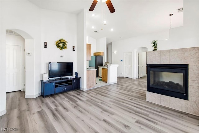 unfurnished living room with light wood-style flooring, visible vents, ceiling fan, arched walkways, and a tile fireplace