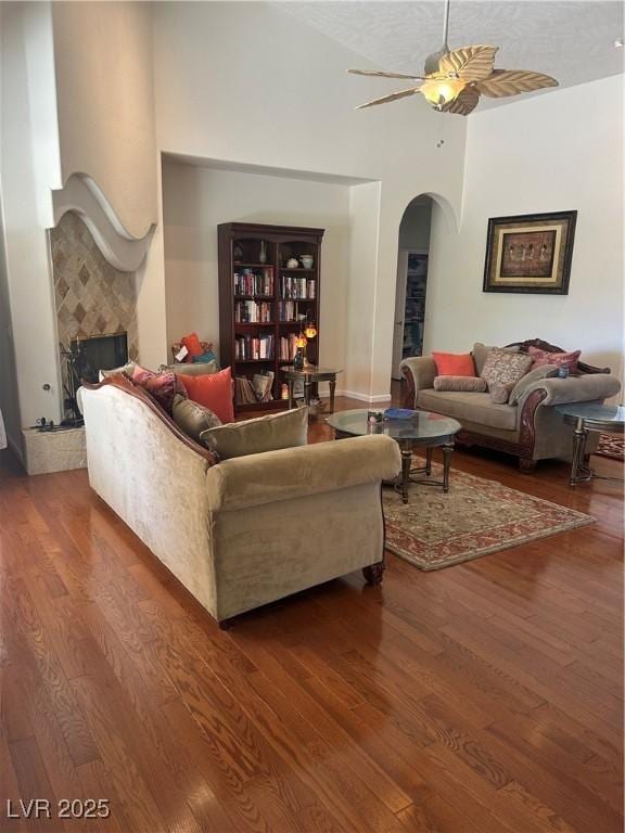 living room with a high ceiling, arched walkways, ceiling fan, and wood finished floors