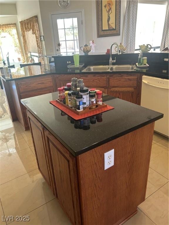 kitchen featuring light tile patterned floors, brown cabinets, dishwasher, a sink, and a center island