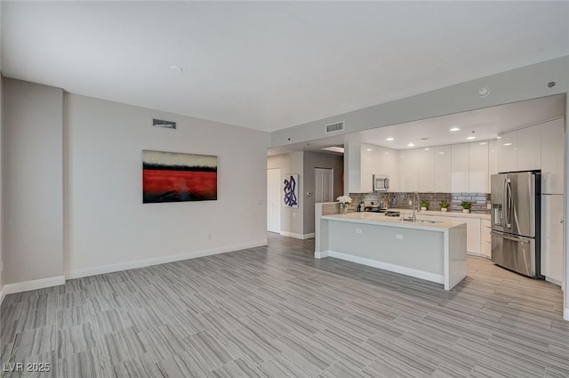 kitchen with appliances with stainless steel finishes, light countertops, backsplash, visible vents, and open floor plan