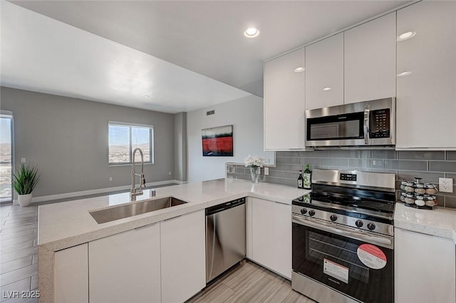 kitchen featuring a sink, stainless steel appliances, backsplash, a peninsula, and white cabinetry