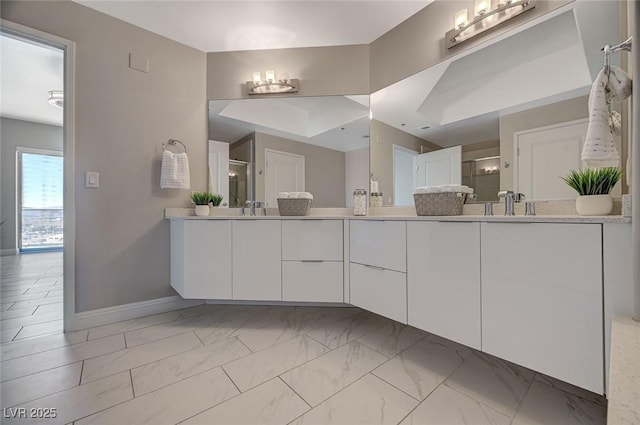 bathroom featuring a shower stall, double vanity, marble finish floor, a sink, and baseboards