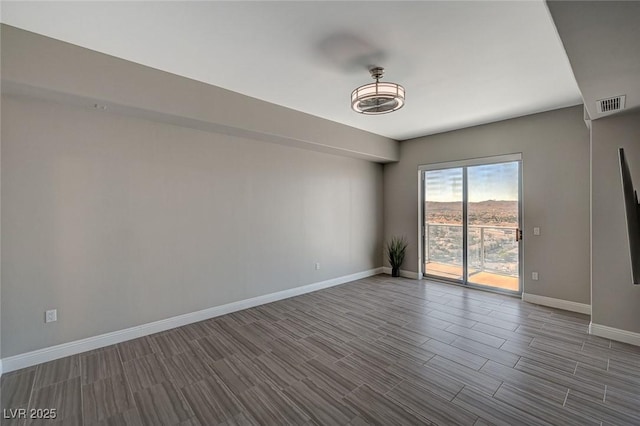 empty room featuring wood finish floors, visible vents, and baseboards
