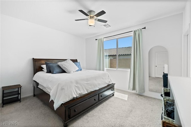 bedroom featuring visible vents, a ceiling fan, arched walkways, and light carpet