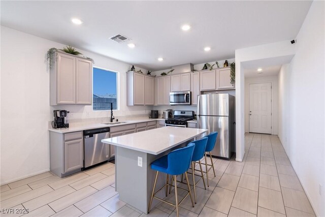 kitchen featuring a kitchen breakfast bar, a sink, visible vents, stainless steel appliances, and a kitchen island