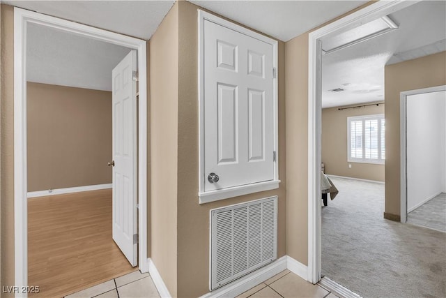 hall with visible vents, baseboards, and tile patterned flooring