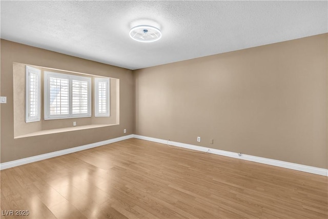 empty room with baseboards, a textured ceiling, and light wood-style flooring