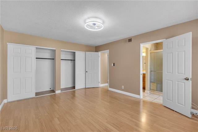 unfurnished bedroom with ensuite bath, light wood-style floors, multiple closets, baseboards, and visible vents