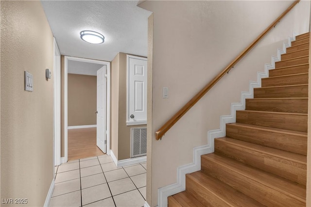 stairway with baseboards, tile patterned flooring, a textured ceiling, and visible vents