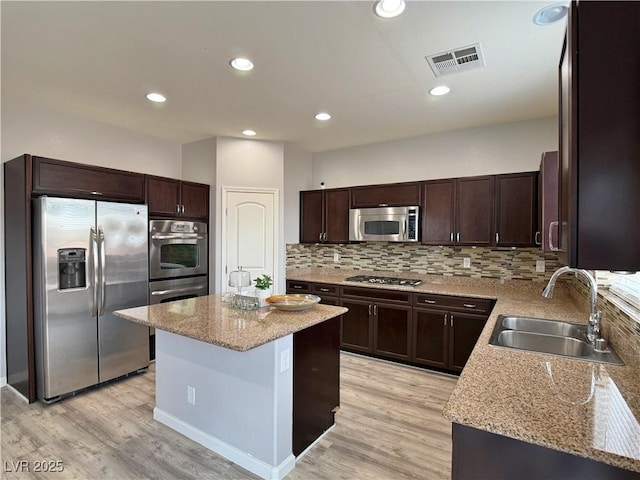kitchen featuring dark brown cabinetry, appliances with stainless steel finishes, a sink, a center island, and visible vents