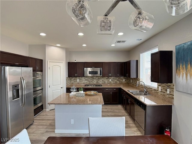 kitchen featuring a kitchen island, backsplash, appliances with stainless steel finishes, light stone countertops, and a sink