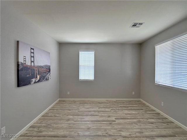 empty room featuring baseboards, wood finished floors, and visible vents