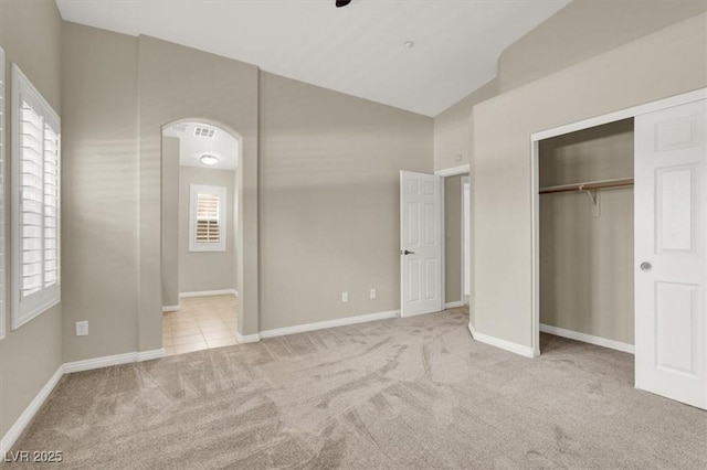 unfurnished bedroom with arched walkways, baseboards, high vaulted ceiling, a closet, and carpet flooring