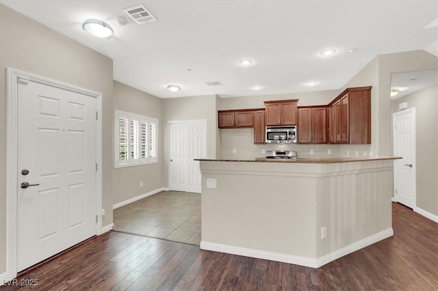 kitchen featuring baseboards, stainless steel microwave, dark wood finished floors, and brown cabinetry