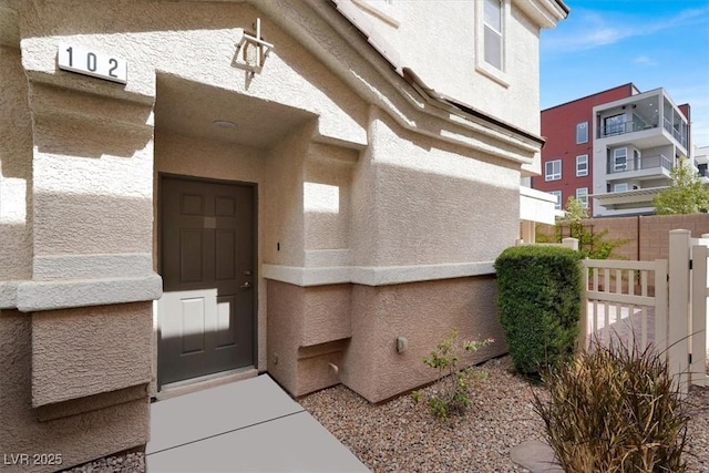 view of exterior entry with fence and stucco siding