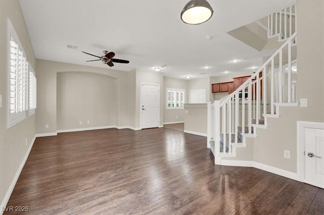 unfurnished living room with ceiling fan, stairs, baseboards, dark wood-type flooring, and visible vents